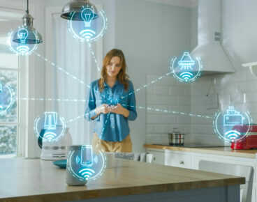 Internet of Things Concept: Young Woman Using Smartphone in Kitchen. She controls her Kitchen Appliances with IOT. Graphics Showing Digitalization Visualization of Connected Home Electronics Devices